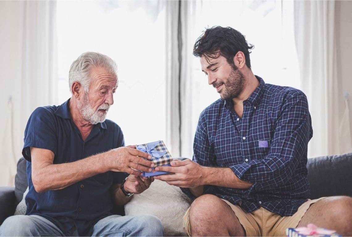 An older man and a younger man looking at a card together on a sofa