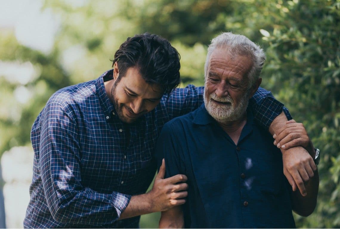 A younger man with his arm around an older man, both laughing